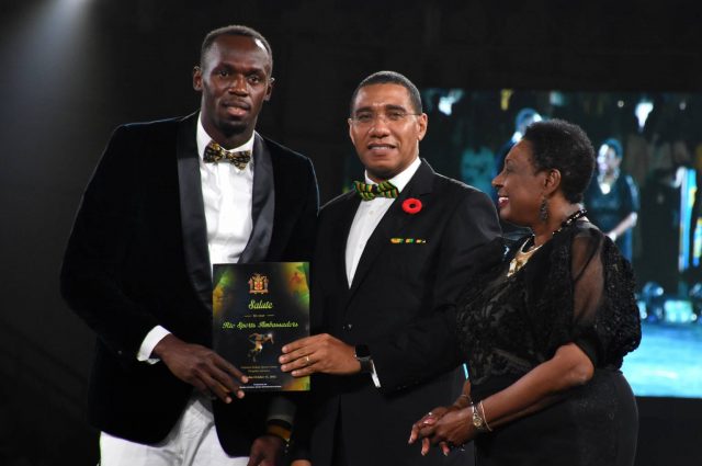 Prime Minister, the Most Hon. Andrew Holness (centre), presents an award to World and Olympic sprint champion, Usain Bolt (left), at a ceremony to honour the 2016 Rio Olympic athletes, at the National Indoor Sports Centre in Kingston, on October 15. Sharing in the moment at (right) is Culture, Gender, Entertainment and Sport Minister, Hon. Olivia Grange.