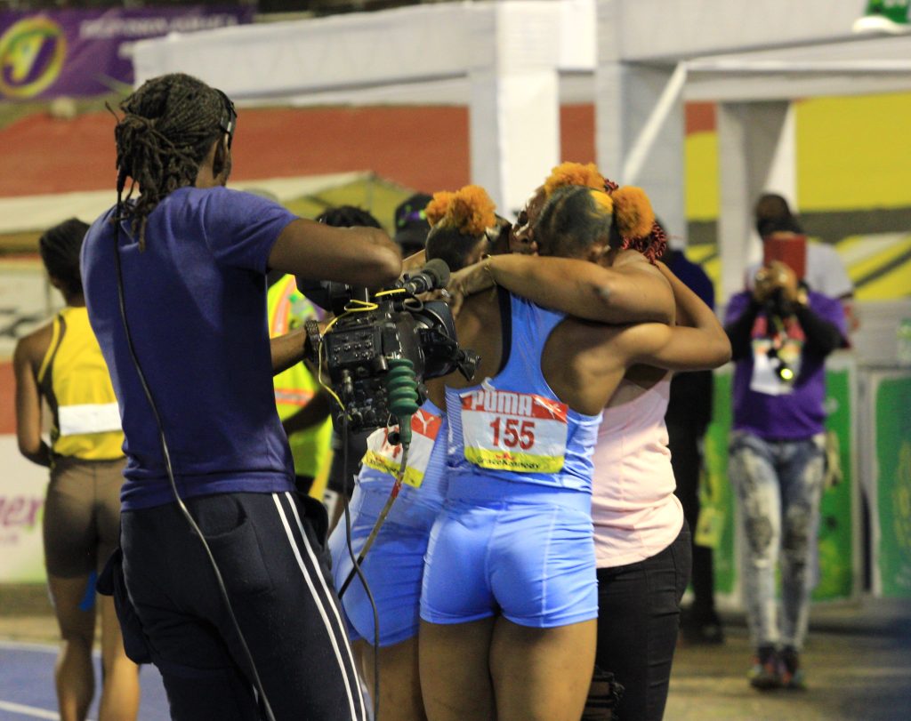 Tina Clayton celebrates with her twin sister Tia and mother after winning the Class 1 girls' 100m final at Champs 2022
