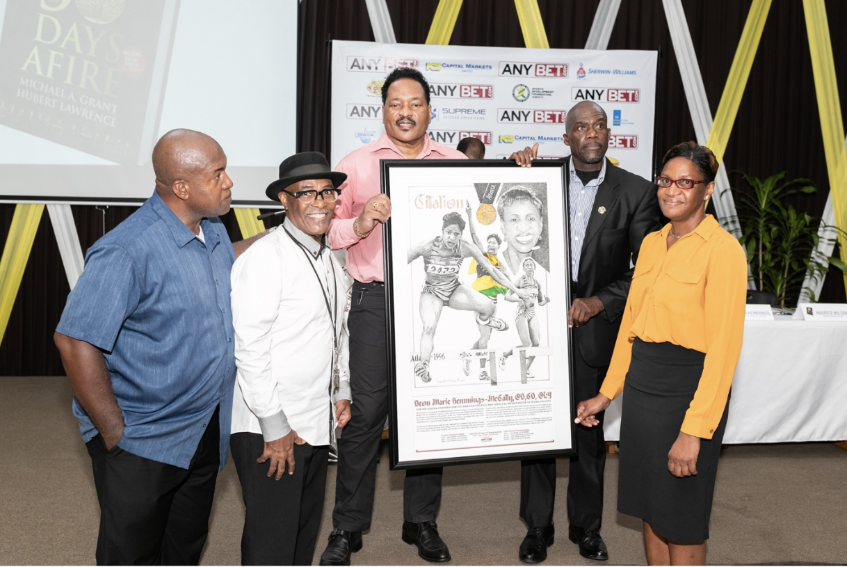 Deon Hemmings-McCatty, Jamaica’s first female Olympic gold medallist, displays the citation awarded to her by AnyBet at the dual launch of the film “Finding Foster” and the book, “Fifty Days Afire” at the GC Foster College Lecture Theatre on Thursday, November 2. Others L-R: Hubert Lawrence, the book’s co-author; artist Patrick Kitson, whose illustration is featured in the citation; Michael A. Grant, co-author and Mr. Gibbs Williams, representing GC Foster College. AnyBet also sponsored components of research and production for the film and book.